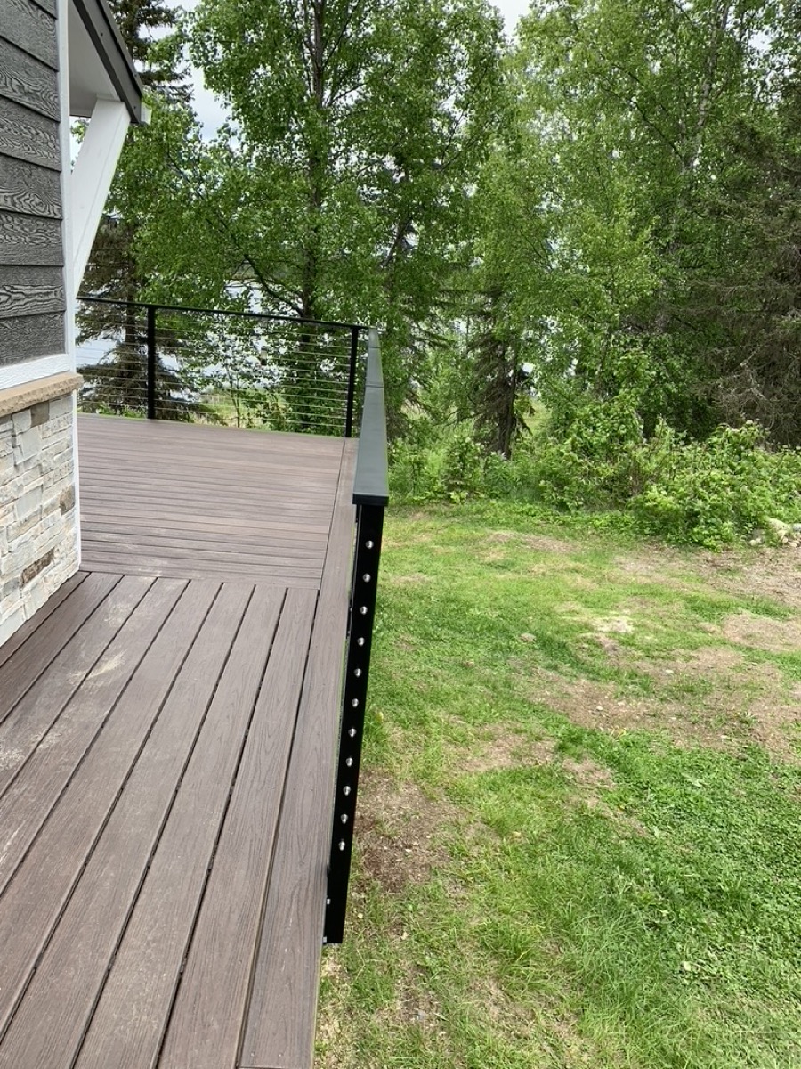 A composite deck corner with a black post and cable railing over grass
