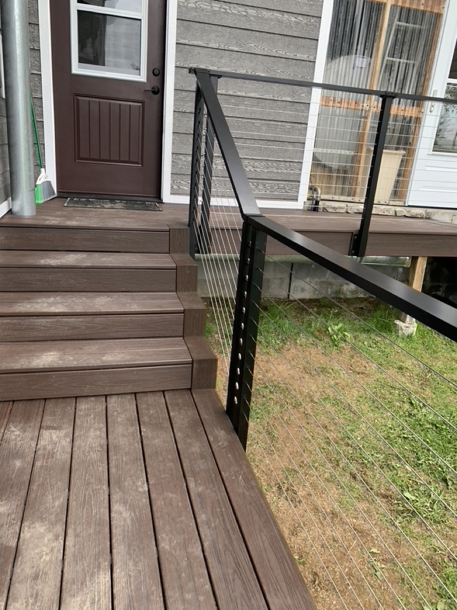 Composite deck steps and cable railing beside a door onto a lawn