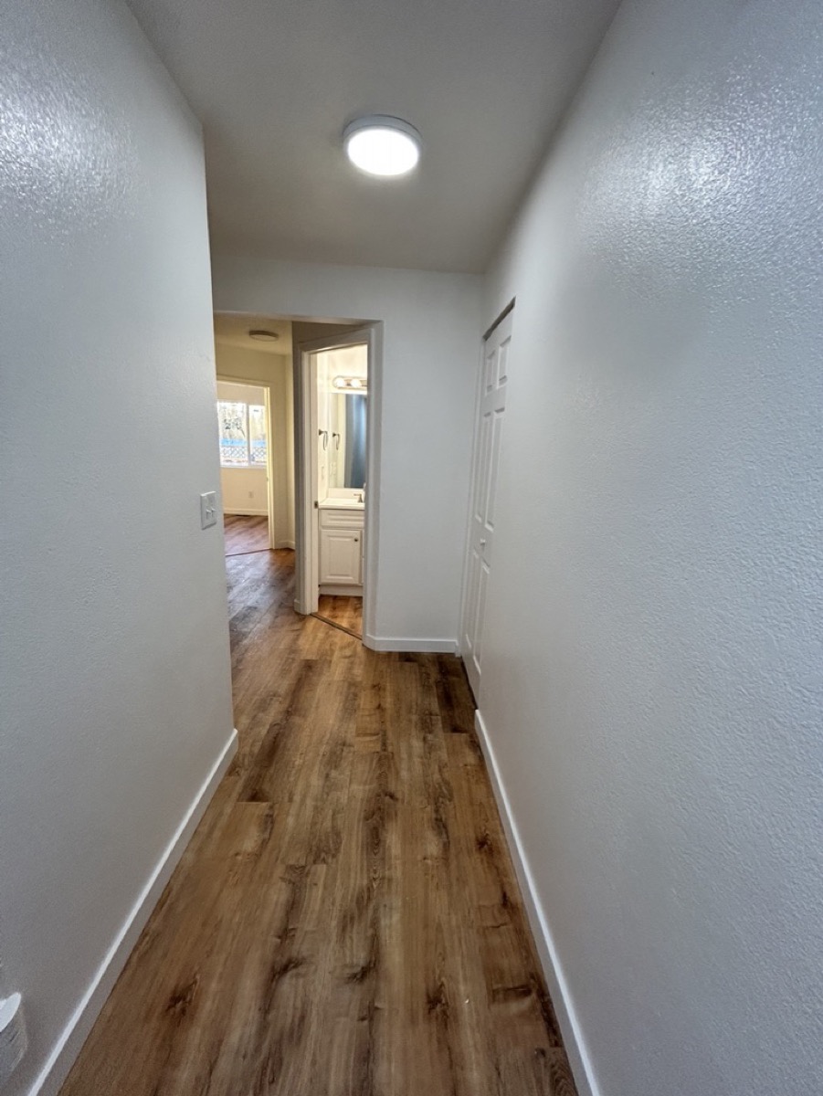 A hallway with finished wood flooring running through to a further room